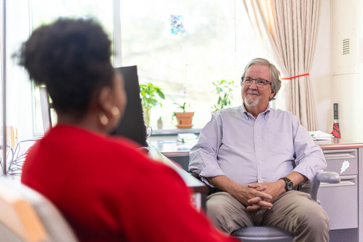 A man from the Student Advocates Office sits at his desk, counseling a student.